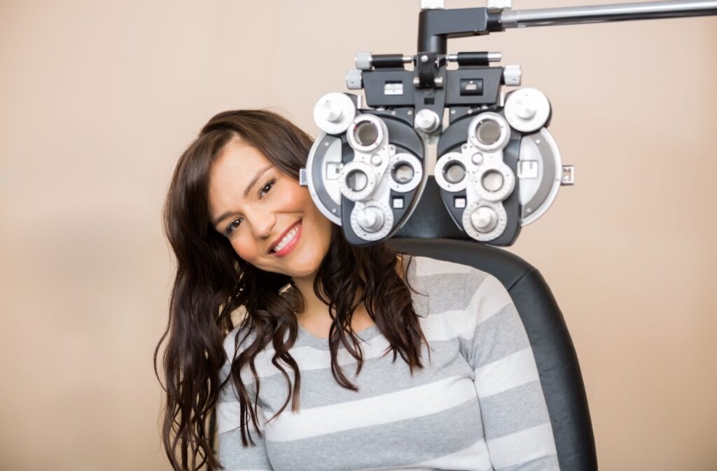 A young patient sitting on the exam chair and smiling behind the phoropter.