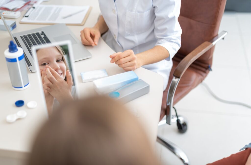 A child practices inserting a contact lens while looking in a mirror at the optometrist’s office.