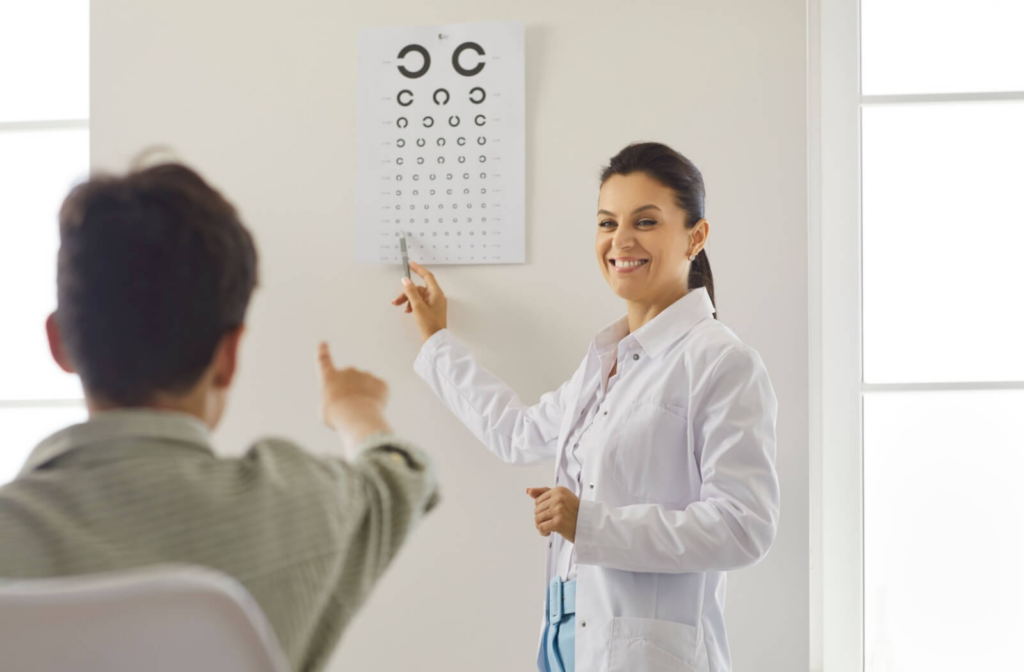 An optometrist points to an eye chart while a patient identifies letters during a vision test.